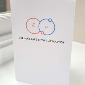 May include: A white greeting card with a red and blue graphic of two overlapping circles. The red circle says "You" and the blue circle says "ME". The text "OUR BOND GOES BEYOND ATTRACTION" is written below the circles.