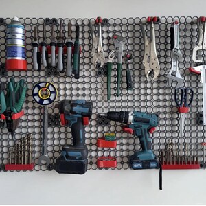 May include: A wall-mounted tool organizer with a variety of hand tools, power tools, and accessories. The tools are arranged on a black pegboard with red and black holders. Includes screwdrivers, wrenches, pliers, drills, and a hammer.