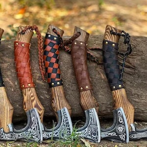 May include: Six Viking axes with wooden handles and ornate silver blades. The handles are wrapped in black, brown, and red leather with decorative studs. The axes are displayed against a weathered log.