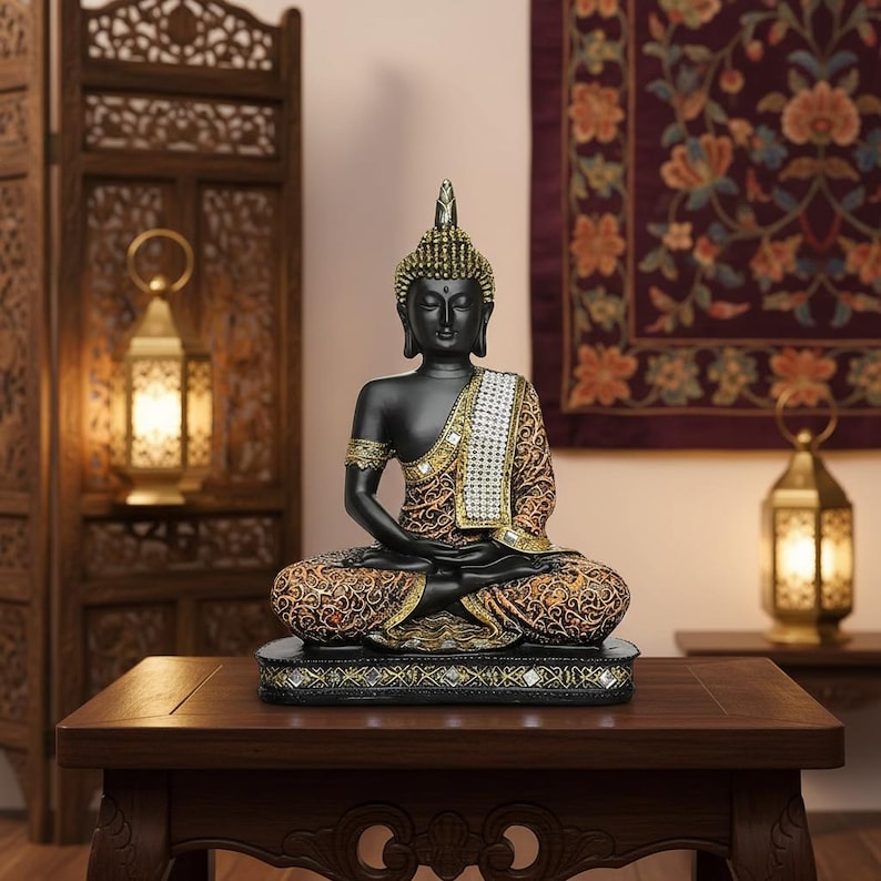 K&ouml;nnte beinhalten: Eine schwarze Buddha-Statue in sitzender Meditationshaltung. Die Statue hat goldene Akzente an Kopf, Armen und Kleidung. Die gemusterte Kleidung ist braun und goldfarben. Die Statue steht auf einem dekorativen Sockel.