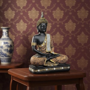 K&ouml;nnte beinhalten: Eine schwarze Buddha-Statue in sitzender Meditationshaltung. Die Statue hat goldene Akzente an Kopf, Armen und Gewand. Das Gewand hat ein detailliertes Muster. Die Statue steht auf einem schwarzen Sockel mit goldenen Verzierungen. Im Hintergrund ist eine Vase zu sehen.