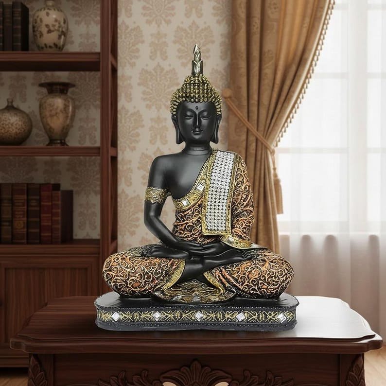 K&ouml;nnte beinhalten: Eine schwarze Buddha-Statue in sitzender Meditationshaltung. Die Statue hat goldene Akzente an Kopf, Armen und Gewand. Das Gewand weist ein detailliertes Muster auf. Die Statue steht auf einem dekorativen Sockel mit Gold- und Schwarzdesign. Die Statue steht auf einem dunklen Holztisch.
