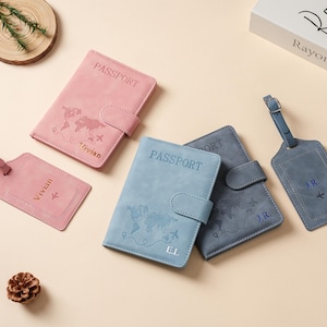 May include: Three passport holders and two luggage tags in pink, light blue, and dark blue. Each item features a world map print, the word PASSPORT, and personalized initials or names including Vivian, E.L., and J.R. with small airplane icons.