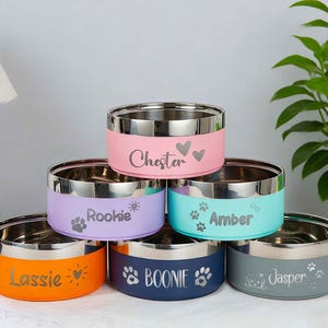 May include: A stack of six stainless steel pet bowls with colored exteriors. Each bowl has a different color: orange, navy, gray, pink, purple, and teal. Each bowl is personalized with a pet's name and paw print or heart design.