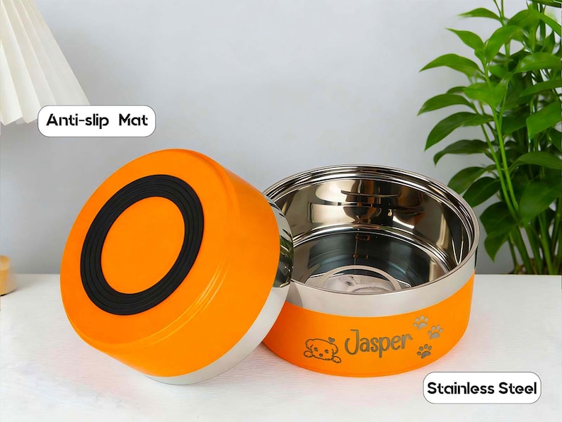 May include: An orange and stainless steel pet food bowl with the name "Jasper" and paw prints. The bowl has a black anti-slip mat on the lid. The words "Anti-slip Mat" and "Stainless Steel" are also visible.