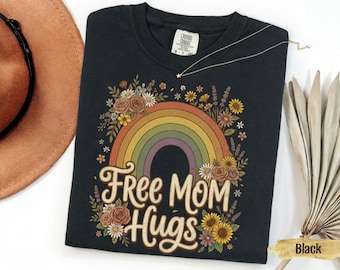 May include: Black t-shirt with a rainbow and floral design. The shirt features the text "Free Mom Hugs" in a vintage font. The rainbow has multiple colors, and the flowers are in shades of yellow, orange, and brown.