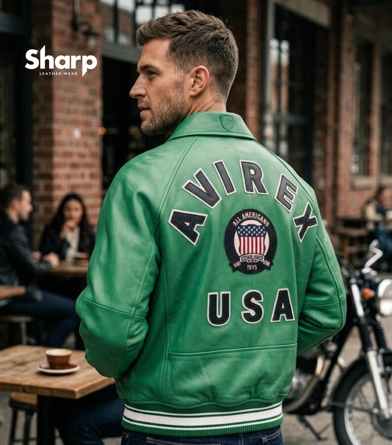 May include: A green leather jacket with the word "AVIREX" across the back, along with a patch featuring the American flag and the word "USA". The jacket has a white and blue striped hem and cuffs.