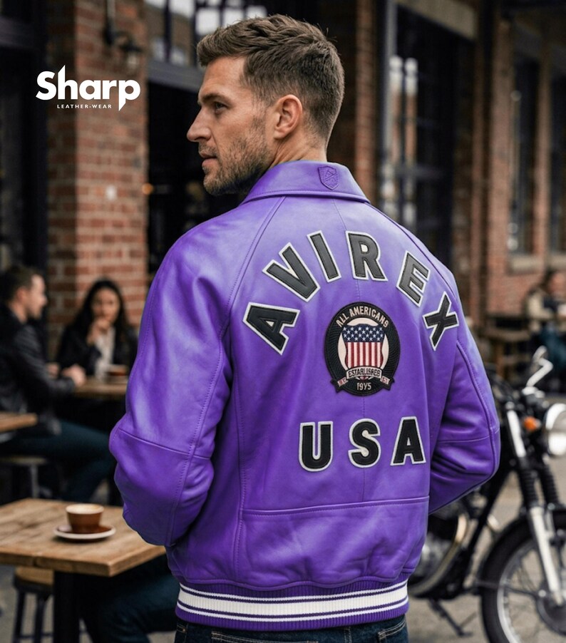 May include: A purple leather jacket with the word "AVIREX" across the back, along with a patch featuring the American flag and the text "ALL AMERICANS" and "USA". The jacket has a white and navy blue striped trim at the waist and cuffs.
