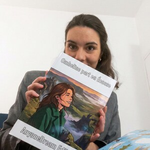 Peut inclure: Un livre intitulé "Ombeline part en Écosse" avec une illustration de couverture d'une femme en manteau vert, avec le texte "AnyoneDream Edition". Le livre est tenu par une personne. Un cadeau emballé avec un motif de pingouin bleu et blanc est au premier plan.