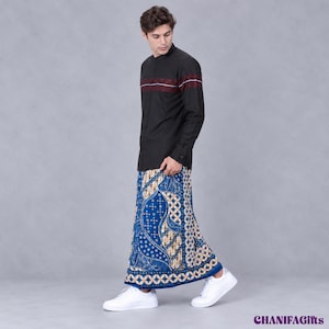 May include: A black long-sleeved shirt with a mandarin collar and a horizontal maroon and white stripe across the chest, paired with a blue sarong featuring a white and gold intricate batik pattern and white sneakers. The text CHANIFAGifts is visible.
