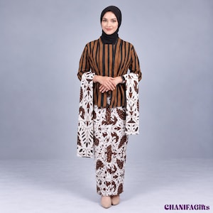 Puede incluir: Una chaqueta de manga larga con rayas verticales marrones y negras combinada con una falda larga a juego con un estampado batik floral en blanco y marrón. Un chal coordinado con el mismo estampado floral cuelga sobre los brazos.