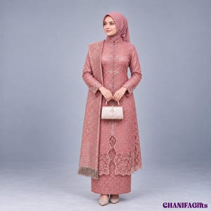 Puede incluir: Un vestido de manga larga en color rosa empolvado con superposiciones de encaje intrincado, cuello alto con botones verticales y un chal a juego con flecos. El conjunto incluye un bolso pequeño, rectangular y estructurado de color claro.
