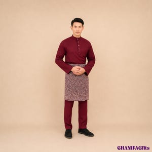 Può includere: Una camicia a maniche lunghe color bordeaux con colletto alla coreana e abbottonatura frontale, abbinata a pantaloni bordeaux coordinati e un sarong a motivi geometrici nei toni del bordeaux e del bianco, indossato sopra i pantaloni.