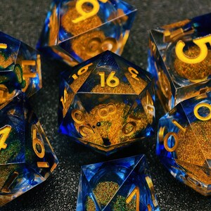 Può includere: Diversi dadi poliedrici con una combinazione di colori blu e oro. I dadi sono trasparenti, con glitter dorati e vortici blu. I numeri sono dorati. Per giochi da tavolo.