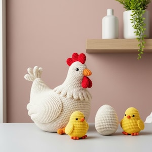 May include: A crocheted white hen with a red comb and wattle, orange beak, and a white egg and two yellow chicks. The hen is the focal point, with the chicks and egg arranged in front. The items are handmade.
