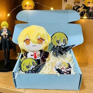 Può includere: Una scatola azzurra piena di merchandising a tema anime. La scatola contiene una bambola di peluche con i capelli gialli, figure in acrilico e una piccola carta. Ulteriori figurine sono esposte sullo scaffale sopra la scatola.