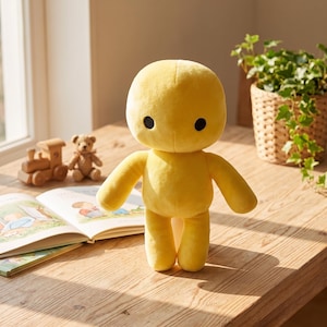 May include: A bright yellow plush doll with a large, rounded head and two small, solid black circular eyes. The doll features a simple, smooth body design with two arms extending to the sides and two legs, standing upright on a wooden surface.