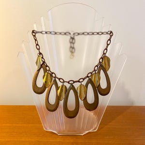 May include: A gold and brown necklace featuring a chain and large teardrop-shaped pendants. The pendants have a cutout design and are accented with smaller gold leaf-shaped charms.