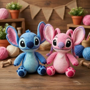 K&ouml;nnte beinhalten: Zwei handgefertigte H&auml;kelpuppen, eine blaue und eine rosa, sitzen nebeneinander auf einer Holzoberfl&auml;che. Die blaue Puppe hat gro&szlig;e Ohren mit rosa Akzenten, w&auml;hrend die rosa Puppe &auml;hnliche Merkmale aufweist. Beide Puppen haben schwarze Augen und sind mit detaillierten N&auml;hten gefertigt.