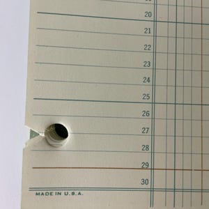 May include: Close-up of a vintage ledger paper with horizontal lines and vertical columns. The paper has two punched holes and the numbers 17 through 30 are visible. The text "MADE IN U.S.A." is printed at the bottom.