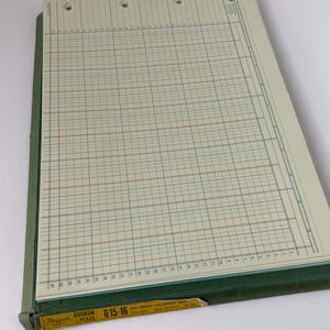 May include: An open ledger book with a green cover and lined pages. The pages are cream-colored with blue and red grid lines. The top of the pages have three holes for binding. A yellow pencil is inserted into the book.