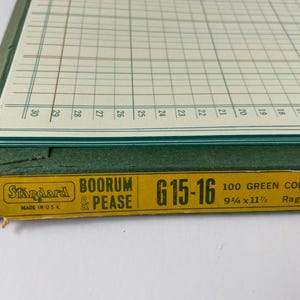 May include: Close-up of a vintage ledger book with a green cover and grid-lined pages. The book has a yellow label with the text "Standard BOORUM & PEASE G15-16" and measurements of 9.25 x 11.875 inches. Made in the USA.