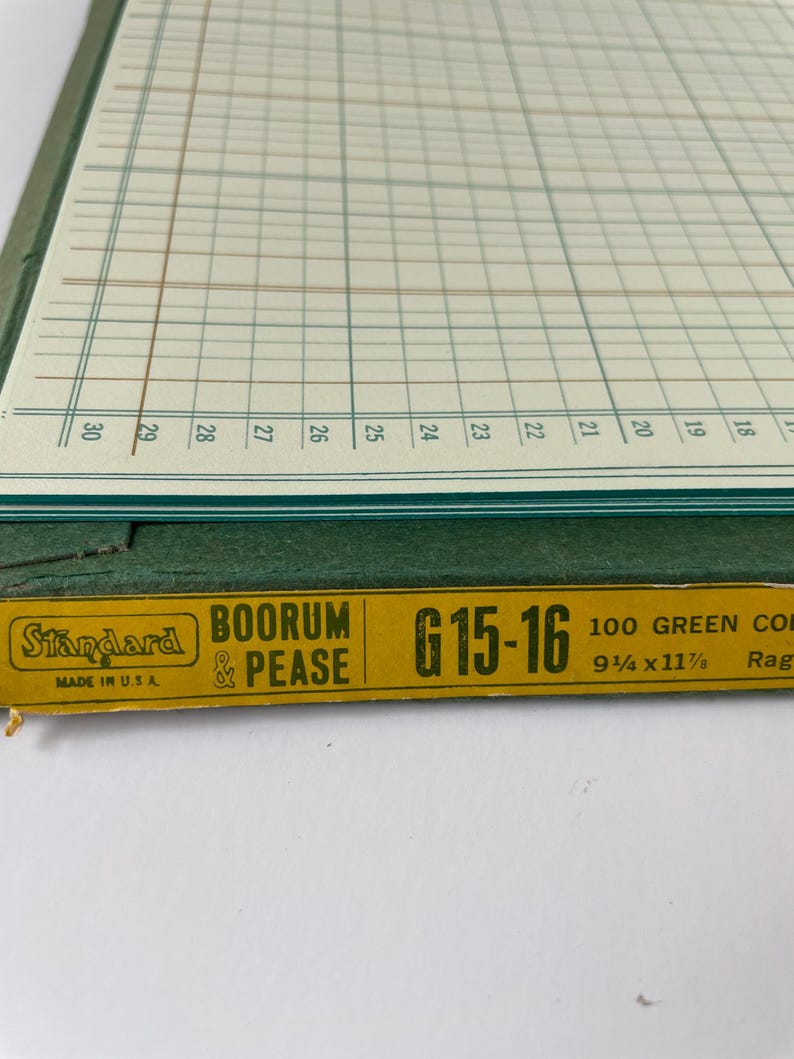 May include: Close-up of a vintage ledger book with a green cover and grid-lined pages. The book has a yellow label with the text "Standard BOORUM & PEASE G15-16" and measurements of 9.25 x 11.875 inches. Made in the USA.