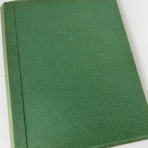 May include: A closed, green book with a textured cover. The spine is a darker shade of green. The bottom corner has a yellow label with black text. The book appears to be vintage or antique.