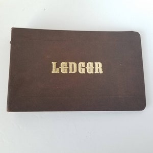 May include: A brown leather-bound ledger with the word "LEDGER" embossed in gold lettering.