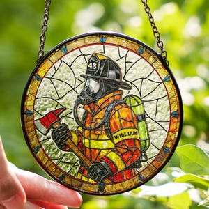 May include: Stained glass round featuring a firefighter in full gear, holding an axe. The firefighter wears a helmet with the number 43, a breathing apparatus, and a name tag that reads "WILLIAM". The piece is framed with a decorative border and a chain for hanging.