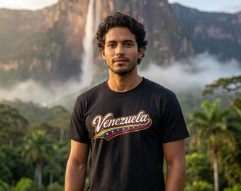 May include: A black short-sleeved t-shirt featuring the word Venezuela in a stylized white script font with a gold outline. Below the text, a graphic element displays the yellow, blue, and red colors of the national flag with white stars.