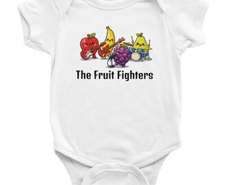 May include: White baby onesie featuring a cartoon band of fruits: an apple playing guitar, a banana on bass, a grape singing, and a pear on drums. The text "The Fruit Fighters" is printed below the band.