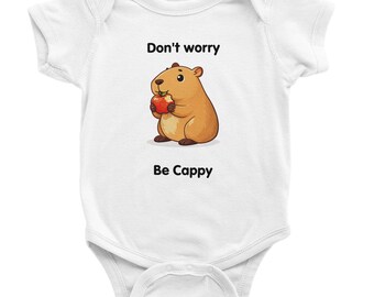 May include: White baby onesie with a cartoon illustration of a brown capybara holding a red apple. The text "Don't worry Be Cappy" is printed above and below the illustration.