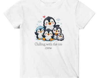 May include: White t-shirt featuring a graphic of five cartoon penguins. The penguins are black and white with orange beaks and feet. The text "Chilling with the ice crew" is below the penguins. The shirt is made of a soft material.