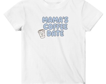 May include: A white short-sleeved t-shirt featuring the text MAMA'S COFFEE DATE in light blue bubble letters. To the left of the text is a small graphic of a coffee cup with a heart outline on the front, rendered in brown and white.
