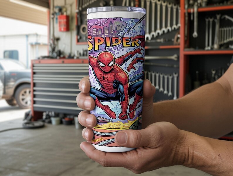 May include: A cylindrical stainless steel tumbler featuring a colorful comic book graphic of a red and blue costumed superhero in a dynamic pose. The design includes the word SPIDER in bold yellow letters against a purple city skyline background.