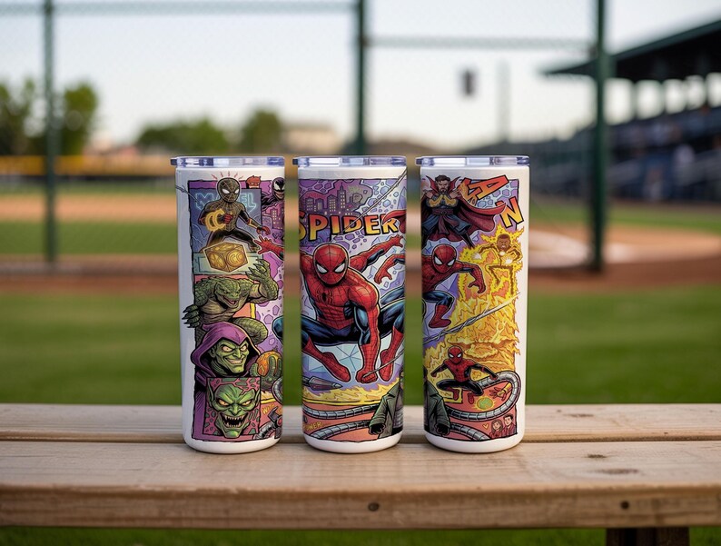 May include: Three cylindrical tumblers with lids featuring a colorful comic book style graphic print. The design displays various characters including Spider-Man, Doctor Strange, and Green Goblin, with the text SPIDER-MAN visible on the surface.
