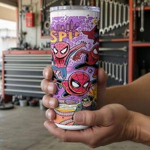 May include: A white tumbler with a comic book design featuring Spider-Man illustrations in red, blue, and black. The design includes the word "SPIDER" in yellow and purple cityscape elements. The tumbler also has the text "great power...great responsibility."