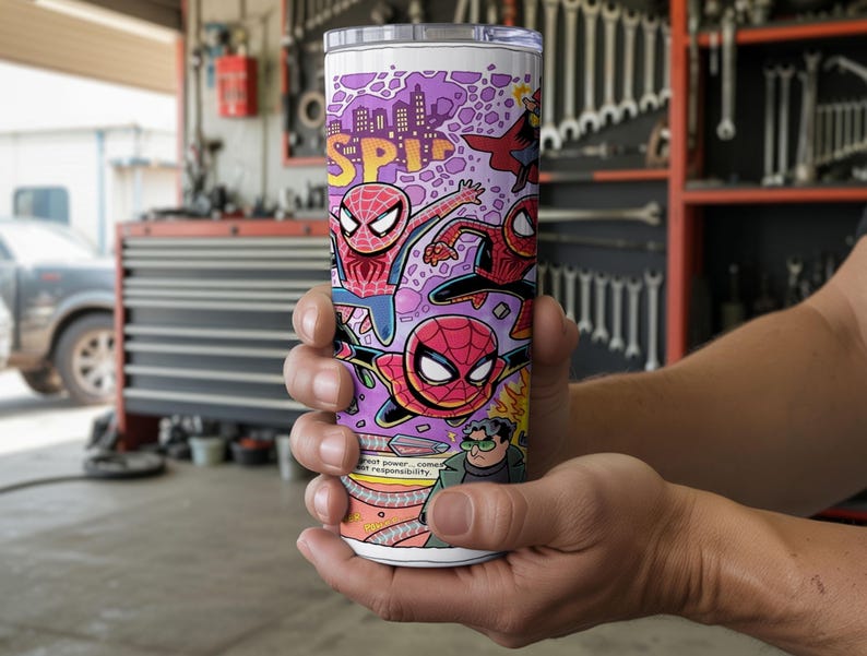 May include: A white tumbler with a comic book design featuring Spider-Man illustrations in red, blue, and black. The design includes the word "SPIDER" in yellow and purple cityscape elements. The tumbler also has the text "great power...great responsibility."