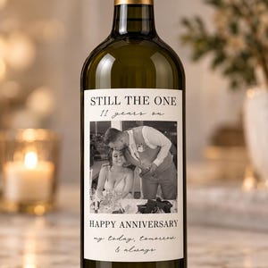 May include: A glass wine bottle with a gold foil cap and a custom white label. The label features a black and white photograph of a couple, with the text STILL THE ONE, 11 years on, HAPPY ANNIVERSARY, and my today, tomorrow & always.