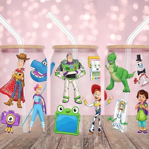 May include: Three clear glass tumblers with bamboo lids and clear straws. Each tumbler features a different Toy Story character design, including Woody, Buzz Lightyear, and Rex. The tumblers are decorated with colorful cartoon graphics.