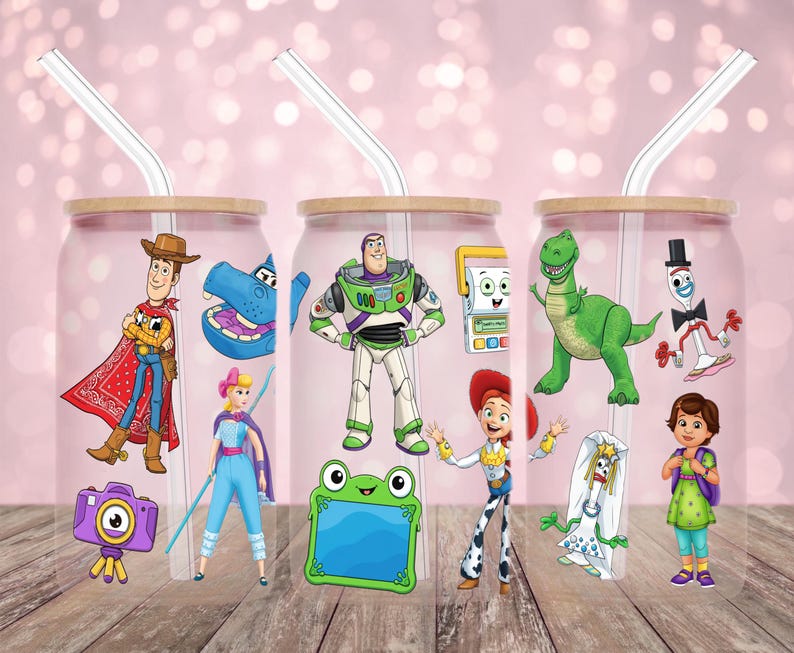 May include: Three clear glass tumblers with bamboo lids and clear straws. Each tumbler features a different Toy Story character design, including Woody, Buzz Lightyear, and Rex. The tumblers are decorated with colorful cartoon graphics.