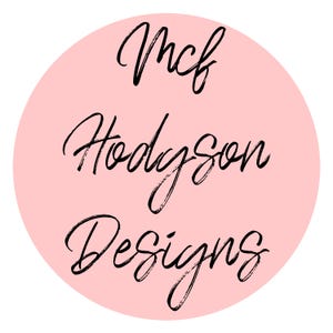 May include: A round, light pink logo with the words "Mcf Hodgson Designs" in black, handwritten-style script. The text is arranged in three lines, centered within the pink circle, against a white background.