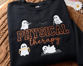 Può includere: Una felpa nera a girocollo con fantasmi bianchi ricamati che eseguono esercizi di fisioterapia. Il testo recita PHYSICAL therapy in lettere arancioni. Il design include piccoli pipistrelli neri e fantasmi che usano un manubrio, un deambulatore, una fascia elastica e un tappetino da yoga.