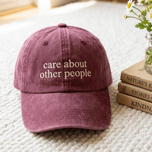 Op de afbeelding: Een kastanjebruine baseballpet met een gewassen, textuurrijke afwerking. Op de voorkant staat de wit geborduurde tekst "care about other people" in een eenvoudig, kleine lettertype met schreef. De pet heeft een gestructureerde kroon en klep.