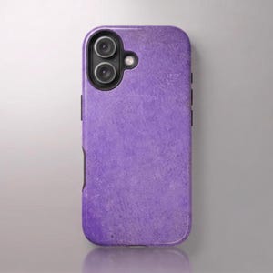 Op de afbeelding: Een rechthoekig smartphonehoesje met een effen, getextureerd paars oppervlak met een gespikkeld uiterlijk. Het hoesje bevat een zwarte cameramodule met twee ronde lenzen en een kleine flitser, geplaatst in de linkerbovenhoek van het toestel.