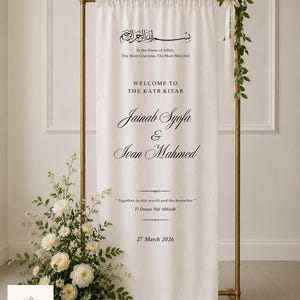 Pode incluir: Uma placa de boas-vindas de casamento em tecido cor de creme pendurada num suporte de metal dourado. A placa apresenta texto a preto que diz "In the Name of Allah," "WELCOME TO THE KATB KITAB," "Jainab Syofa & Ivan Mahmed," e "27 March 2026."