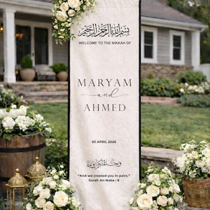 Pode incluir: Uma placa de casamento alta e retangular de tecido cor de creme com texto preto lendo Welcome to the Nikkah of Maryam and Ahmed, 03 April 2026, e And we created you in pairs. É decorada com rosas brancas e folhagens.