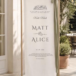 Pode incluir: Uma placa de casamento vertical em tecido branco sujo suspensa numa moldura de madeira clara, com texto a preto incluindo os nomes Matt e Alice, a data 10.09.2026, caligrafia árabe e um verso, acentuada com uma fita verde-azeitona atada no topo.