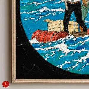 May include: Oil painting of a seascape with a raft and figures. The artwork features a vibrant blue ocean with white waves, a red cylindrical float, and a wooden raft. The painting is framed in a light-colored wooden frame.